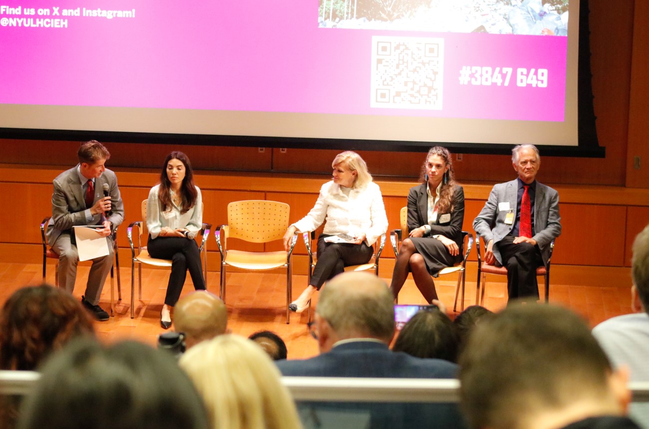 Group of five male and female panelists sit in chairs at the front of an auditorium.
