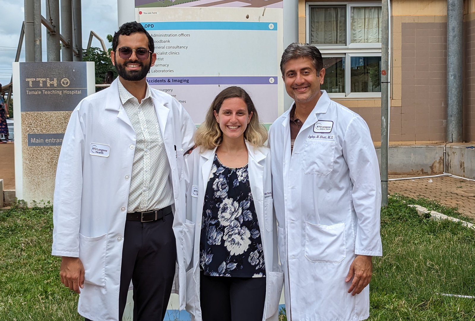Three people wearing white coats and smiling outside of the hospital