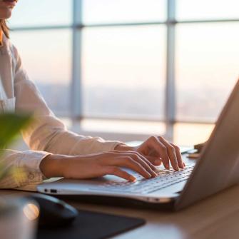 Woman Typing on Laptop in Front of Window