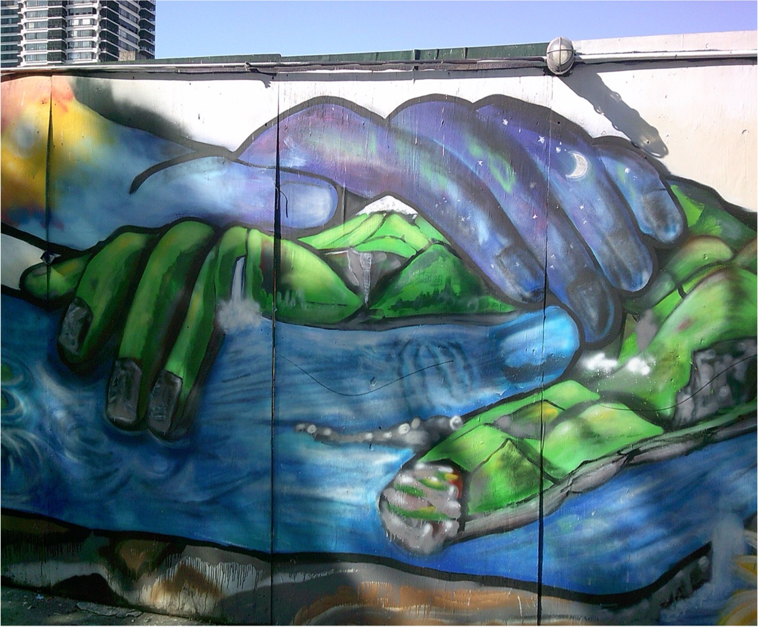 A mural of two large hands holding a landscape with mountains, water, and greenery, under blue sky.