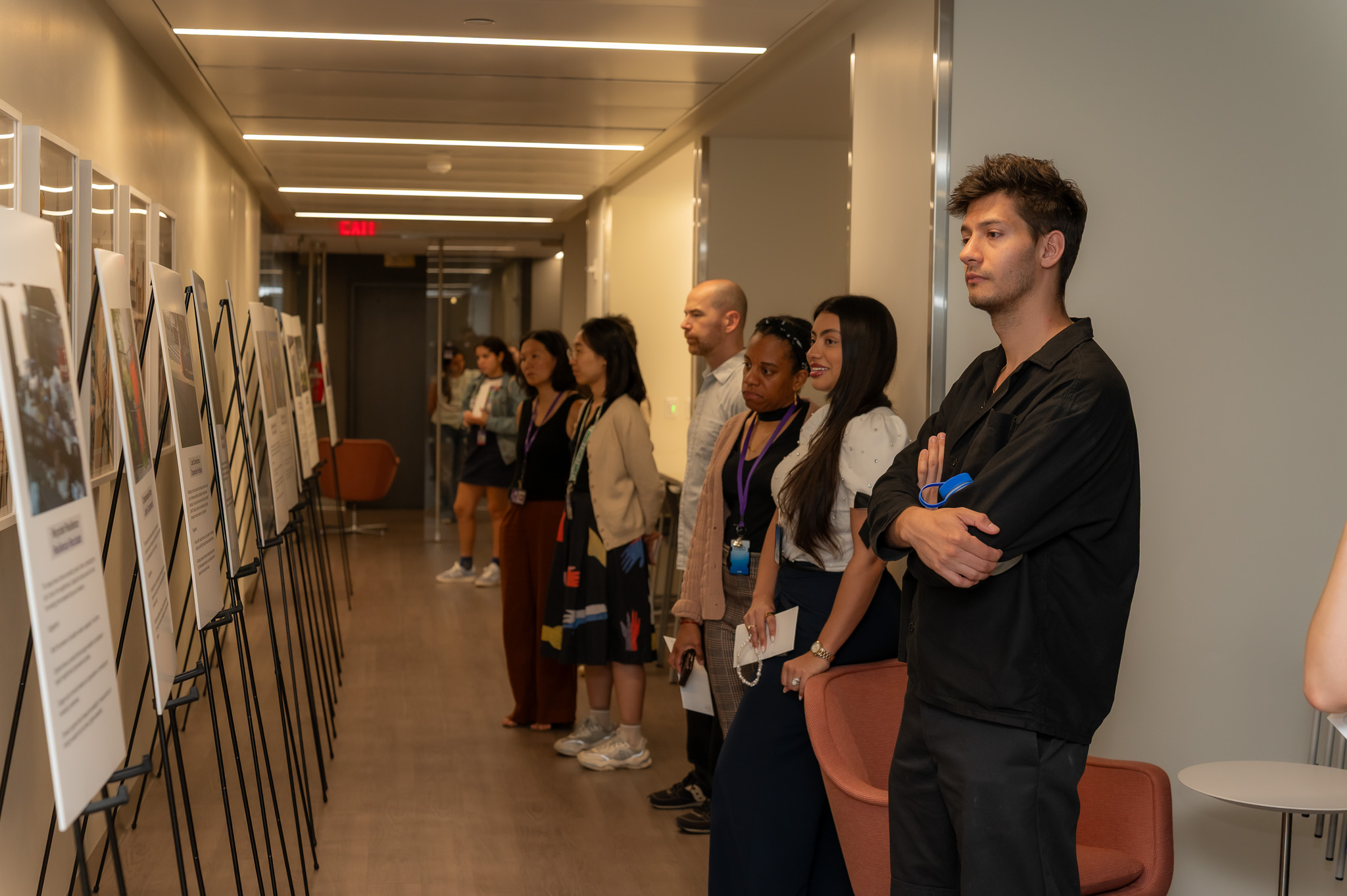 People viewing artwork displayed on easels in a corridor.
