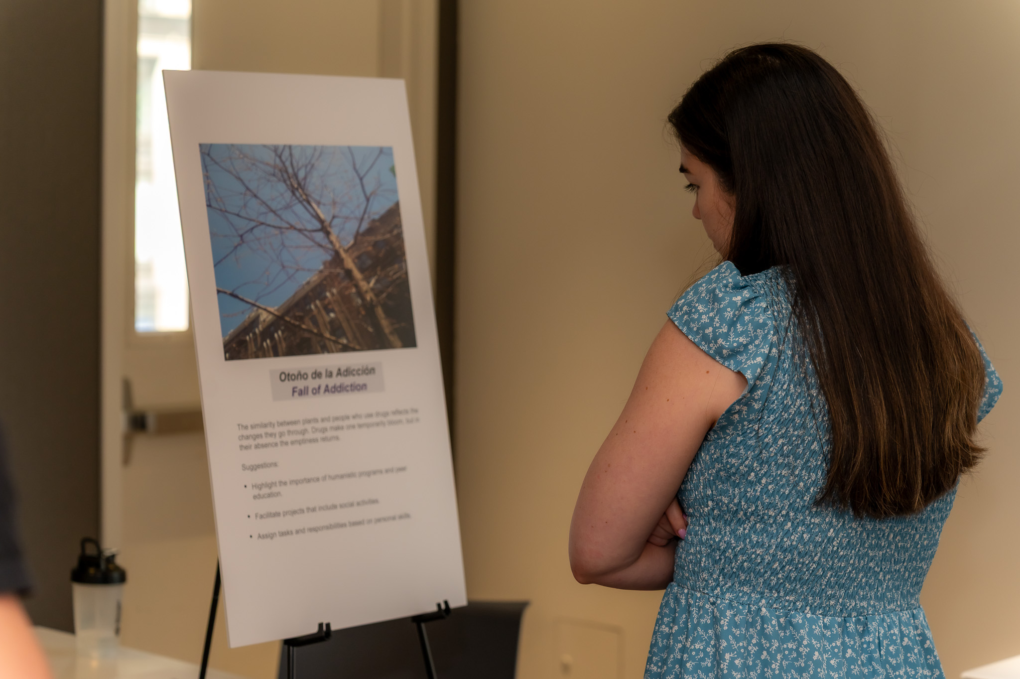 Woman reading text describing photo of a bare tree labeled “Fall of Addiction.