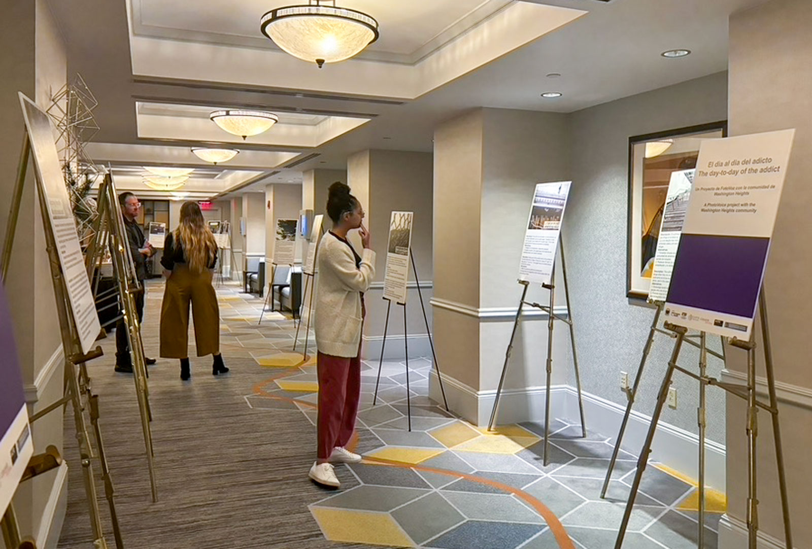 A person views a series of photos placed on easels while two other people talk in the background.